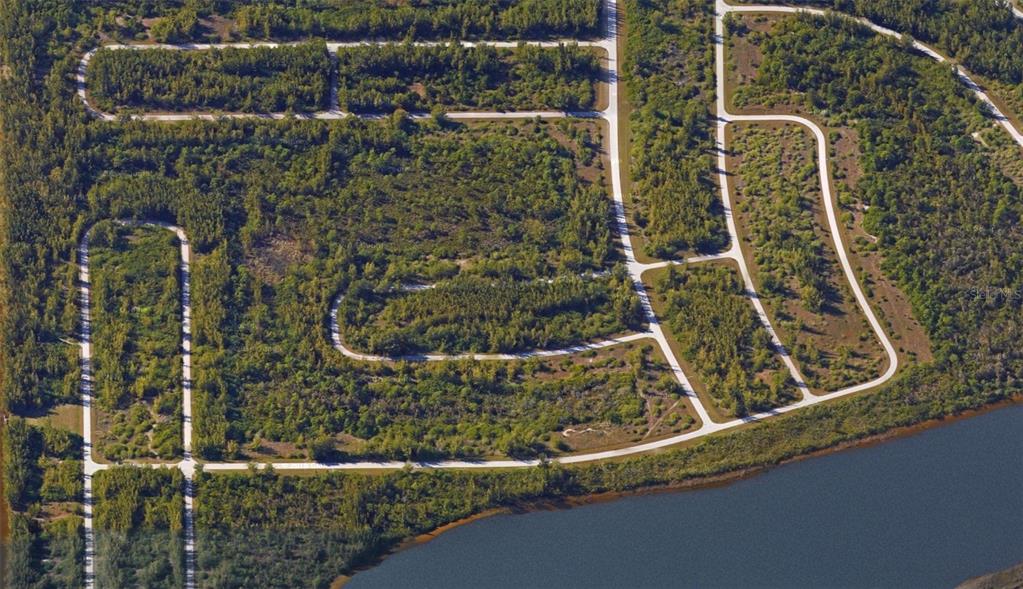 This aerial view shows a vacant residential lot with paved roads surrounded by dense vegetation — 10543 MANGROVE CIRCLE, PORT CHARLOTTE, FL