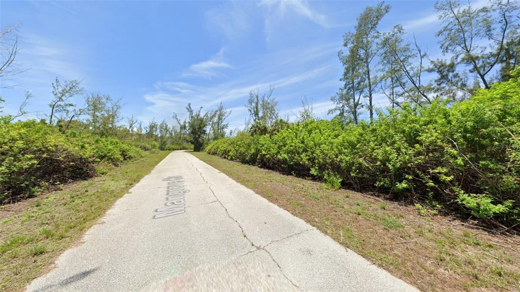 A paved road stretches through a landscape filled with dense green bushes and tall trees — 10543 MANGROVE CIRCLE, PORT CHARLOTTE, FL