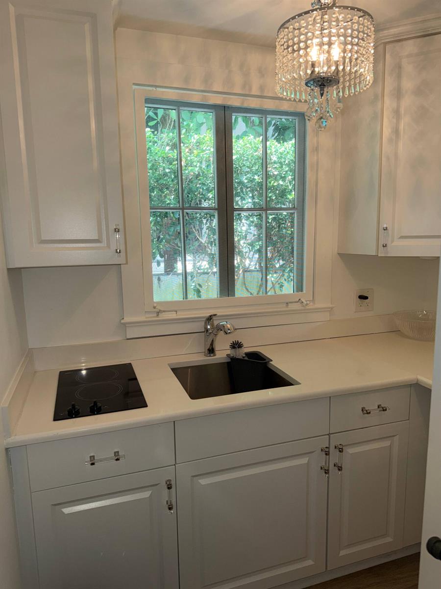 A small kitchen features white cabinets, a black cooktop, a sink, and a crystal chandelier — 301 Chilean Avenue # 0080, Palm Beach FL 33480, PALM BEACH, FL