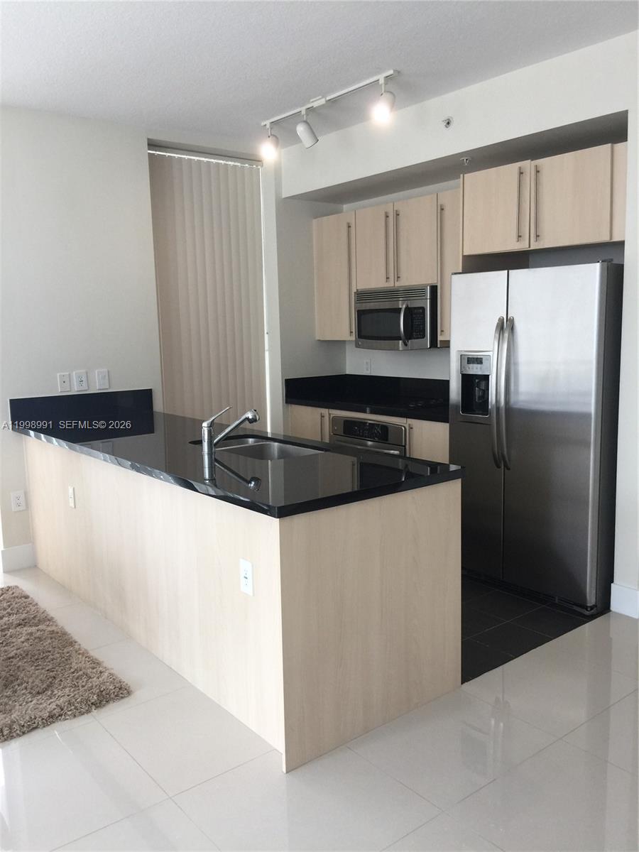 A kitchen features light wood cabinets, black countertops, and stainless steel appliances — 79 SW 12th St, Miami FL 33130, MIAMI, FL