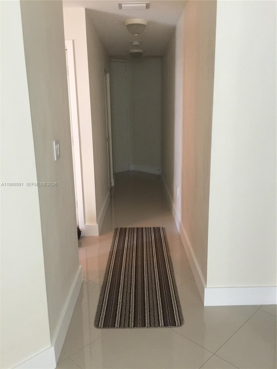 A narrow hallway features light-colored tile flooring, beige walls, and a striped runner rug — 79 SW 12th St, Miami FL 33130, MIAMI, FL