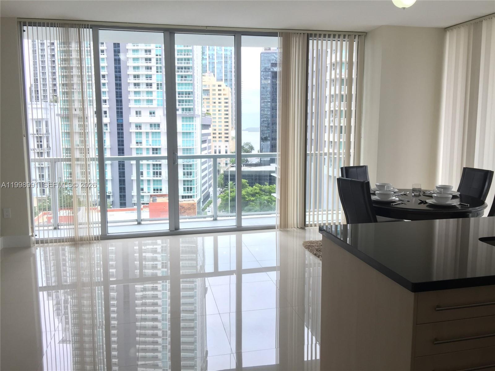 A modern dining area with glossy tile floors overlooks a balcony and city skyline — 79 SW 12th St, Miami FL 33130, MIAMI, FL