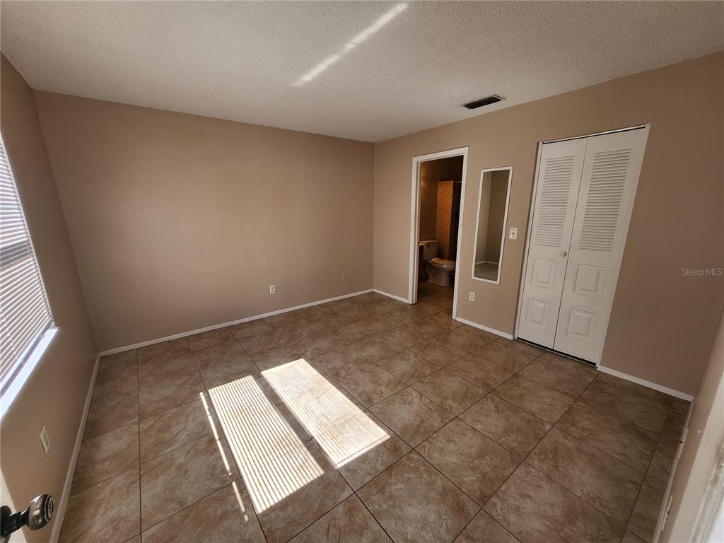 An empty bedroom features tan walls, tiled flooring, a closet, and an attached bathroom — 905 OLD FIELD DRIVE, BRANDON, FL