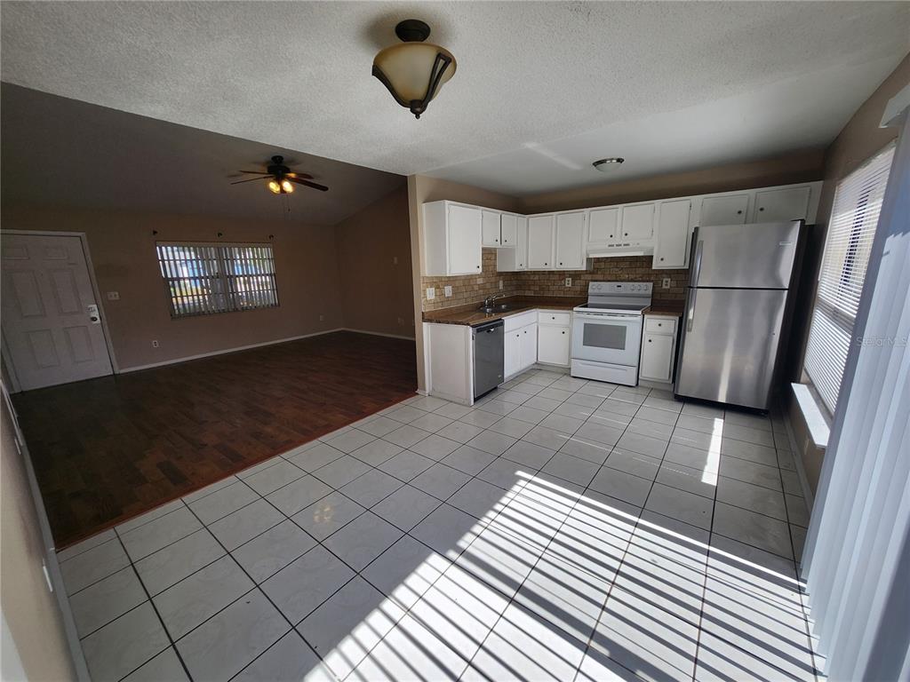 A kitchen with white cabinets and tile flooring opens into a living area with wood floors — 905 OLD FIELD DRIVE, BRANDON, FL