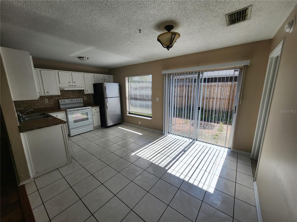 A kitchen with white cabinets, stainless steel appliances, tile flooring, and a sliding glass door — 905 OLD FIELD DRIVE, BRANDON, FL