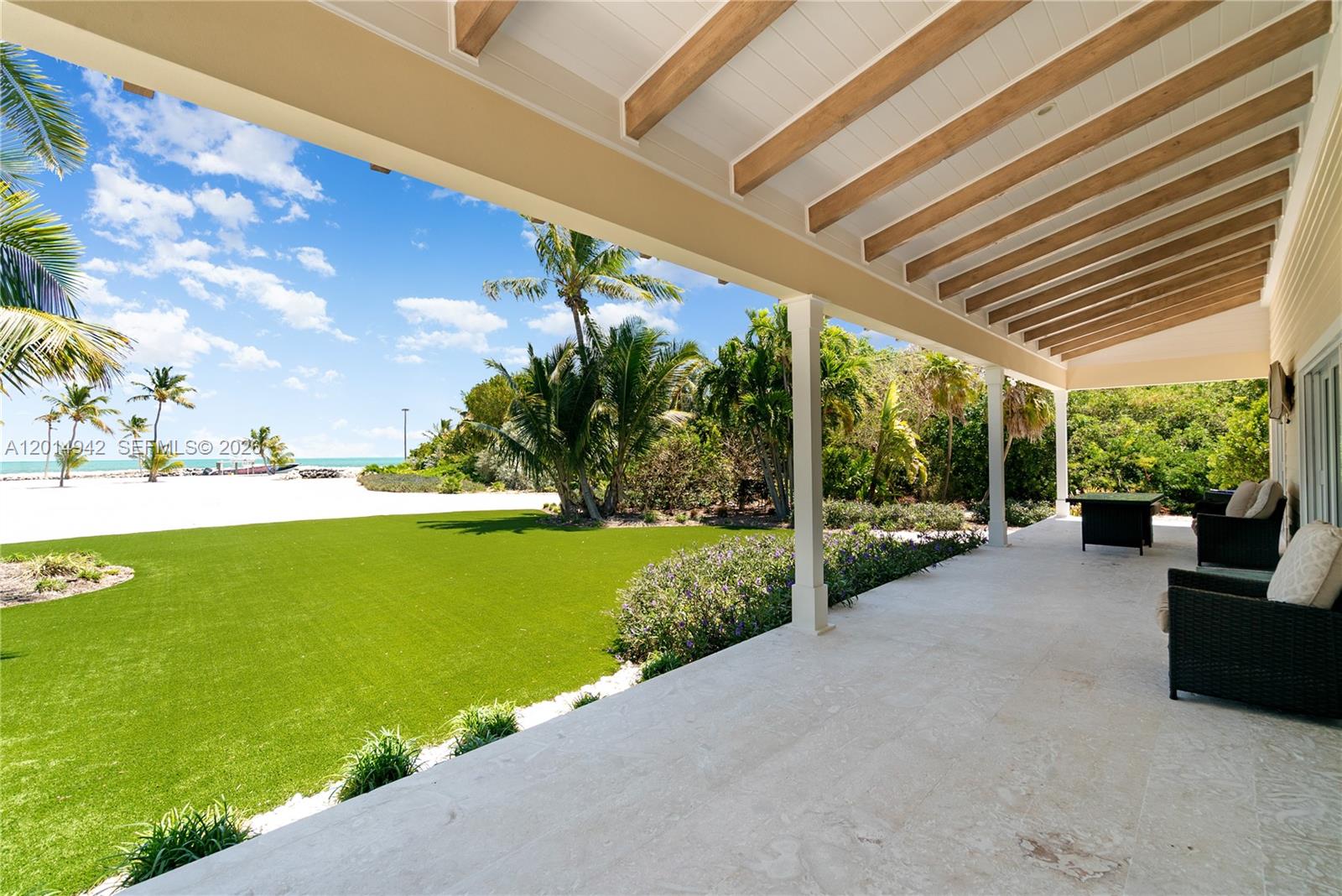 A covered stone patio overlooks a green lawn, palm trees, and a sandy beach — 88835 Old Hwy, Tavernier FL 33070, TAVERNIER, FL