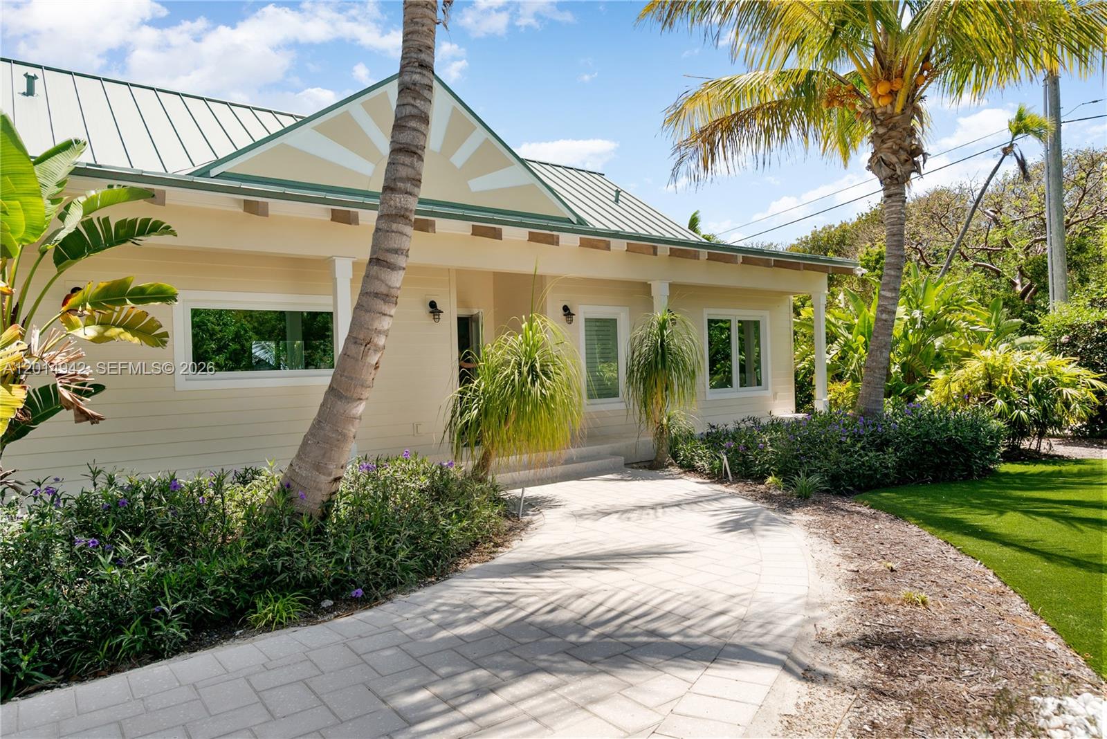 A light-colored house with a metal roof features a paved walkway and tropical landscaping — 88835 Old Hwy, Tavernier FL 33070, TAVERNIER, FL
