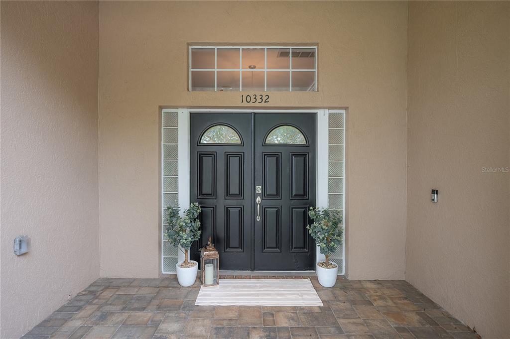 A double front door with glass inserts and a transom window sits under a covered porch — 10332 ABBOTSFORD DRIVE, TAMPA, FL