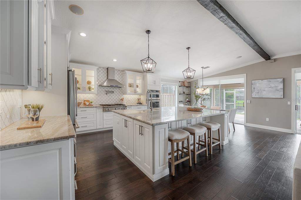 A modern kitchen features white cabinetry, a large granite-topped island, and dark hardwood flooring — 10332 ABBOTSFORD DRIVE, TAMPA, FL