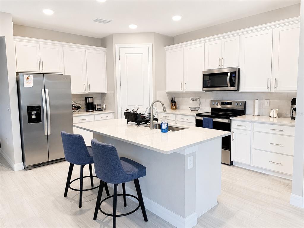 A kitchen features white cabinets, stainless steel appliances, a central island, and blue bar stools — 2635 BEBB OAK DRIVE, NORTH PORT, FL