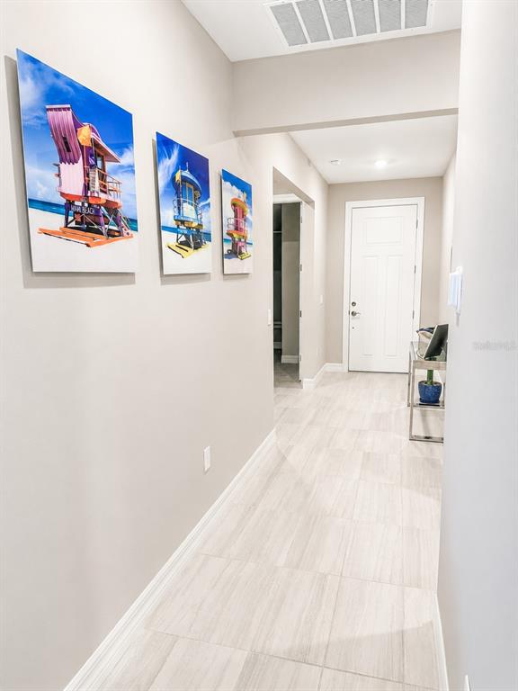 A hallway with light-colored tile flooring features three beach-themed wall art pieces and a door — 2635 BEBB OAK DRIVE, NORTH PORT, FL