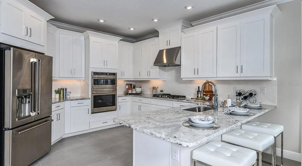 A modern kitchen features white cabinets, stainless steel appliances, and a granite-topped island with seating — 7907 INTERSTELLAR AVENUE, SARASOTA, FL