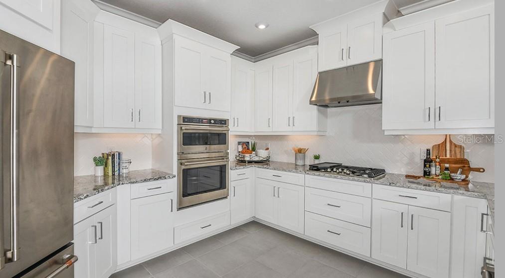 A modern kitchen features white cabinets, stainless steel appliances, granite countertops, and a tile backsplash — 7907 INTERSTELLAR AVENUE, SARASOTA, FL