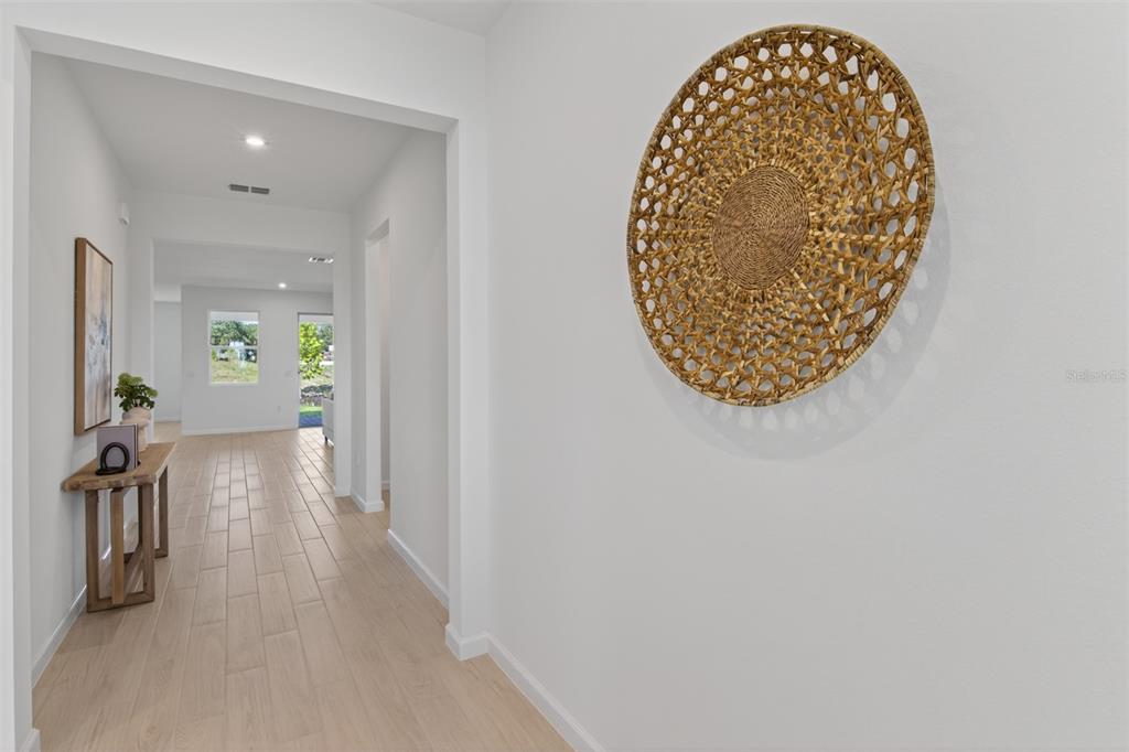 A bright hallway features light wood-look tile flooring, white walls, and a decorative woven wall hanging — 2822 SWEET ACACIA DRIVE, CLERMONT, FL