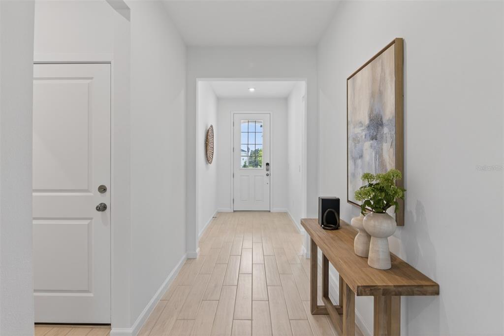 A bright hallway features light wood-look tile flooring, a console table, and a front door — 2822 SWEET ACACIA DRIVE, CLERMONT, FL