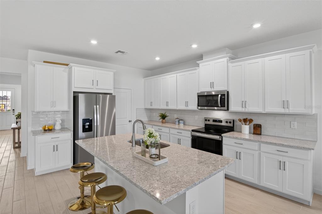 A modern kitchen features white cabinetry, granite countertops, stainless steel appliances, and a central island — 2822 SWEET ACACIA DRIVE, CLERMONT, FL