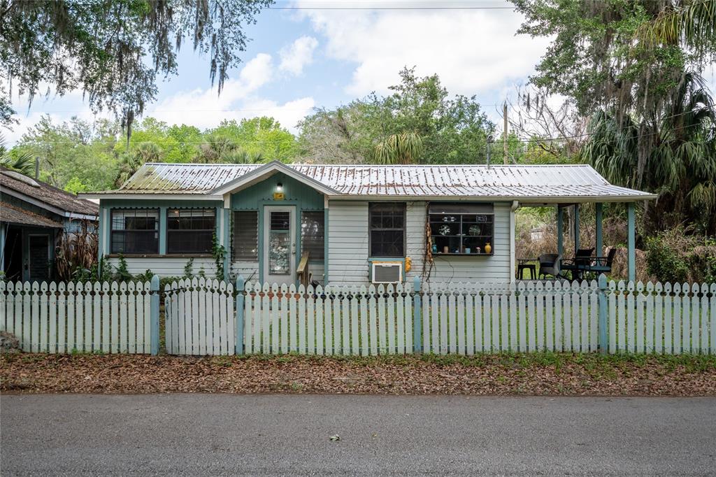 A single-story house with a metal roof and a white picket fence sits outdoors — 5560 PARK AVENUE, DE LEON SPRINGS, FL