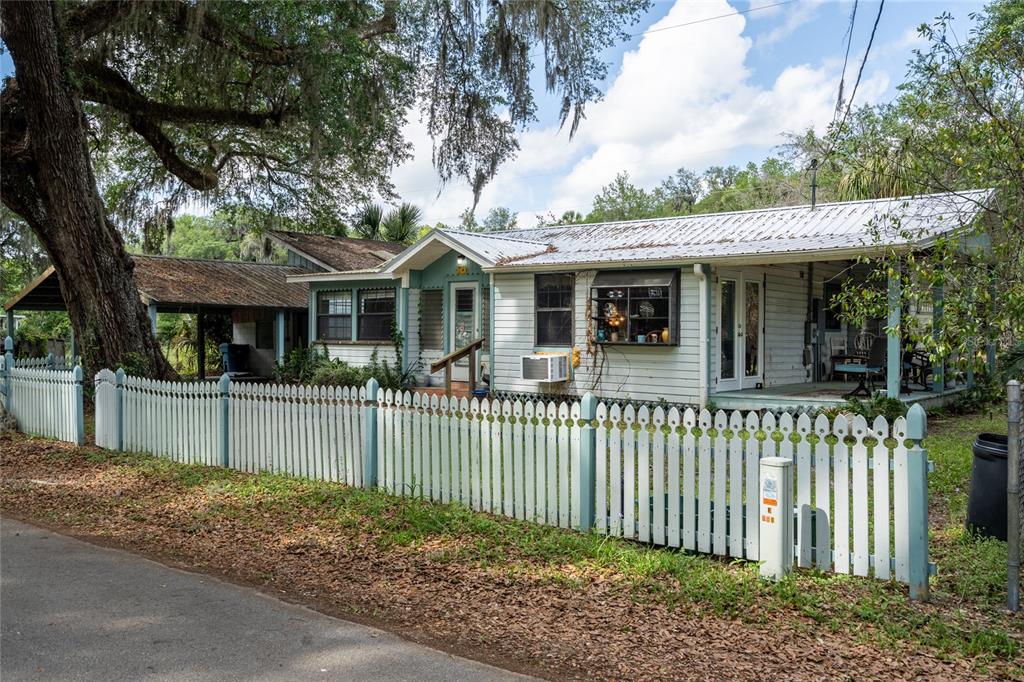 A white house with a metal roof and a picket fence sits under large trees — 5560 PARK AVENUE, DE LEON SPRINGS, FL