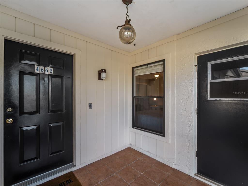 A covered entryway features two black doors, a tiled floor, and a hanging globe light — 4668 OAK HILL LANE UNIT 40, SARASOTA, FL