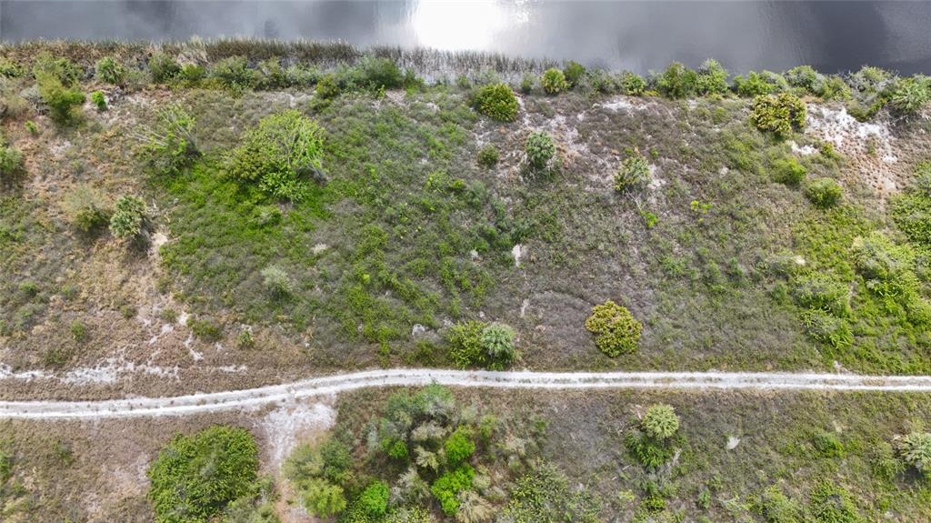 An aerial view shows a dirt path running through a grassy, shrub-filled lot near water — 27399 SOLOMON DRIVE, PUNTA GORDA, FL