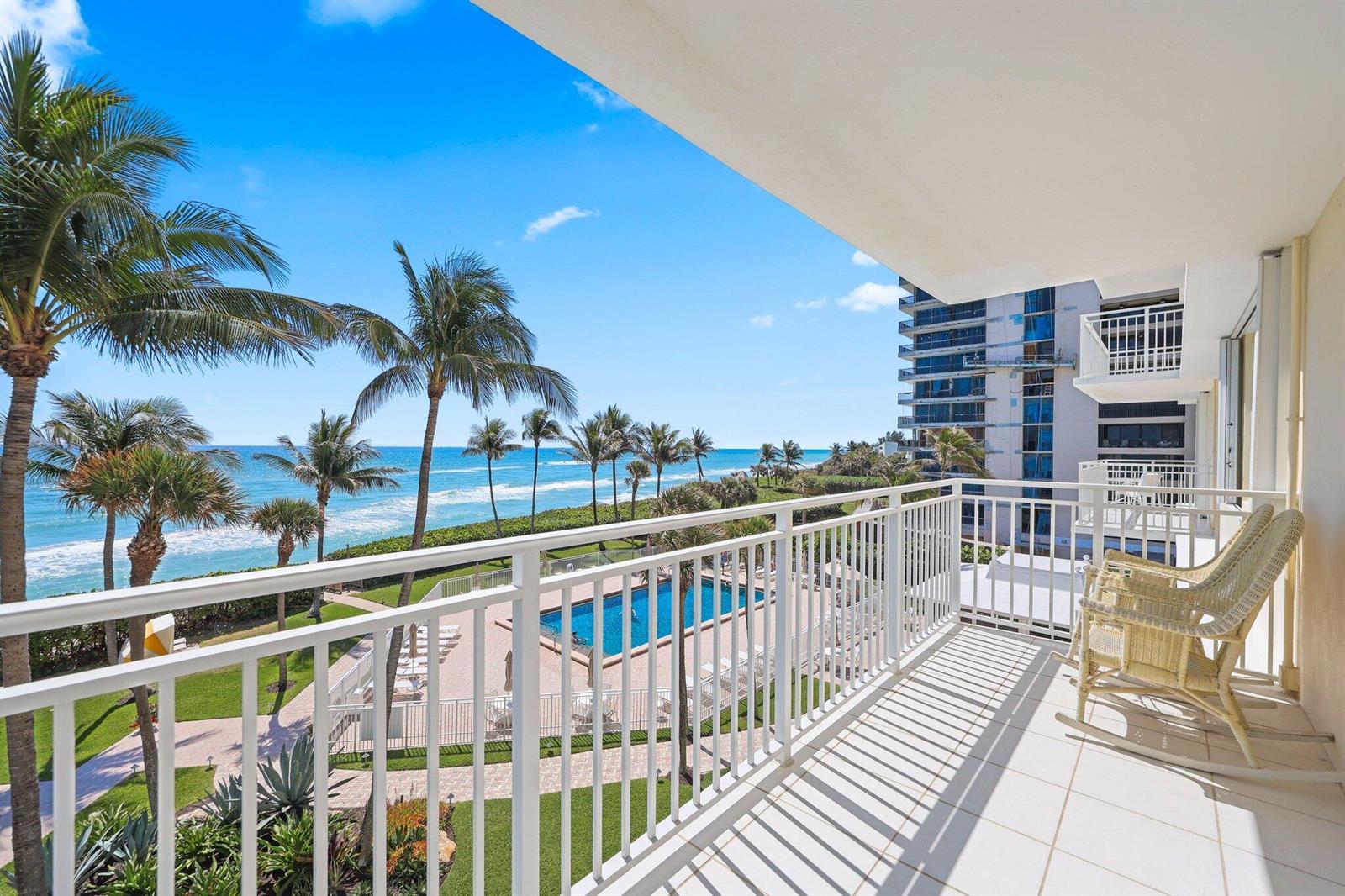 A balcony with white railings overlooks a swimming pool, palm trees, and the ocean — 500 Ocean Drive, Juno Beach FL 33408, JUNO BEACH, FL