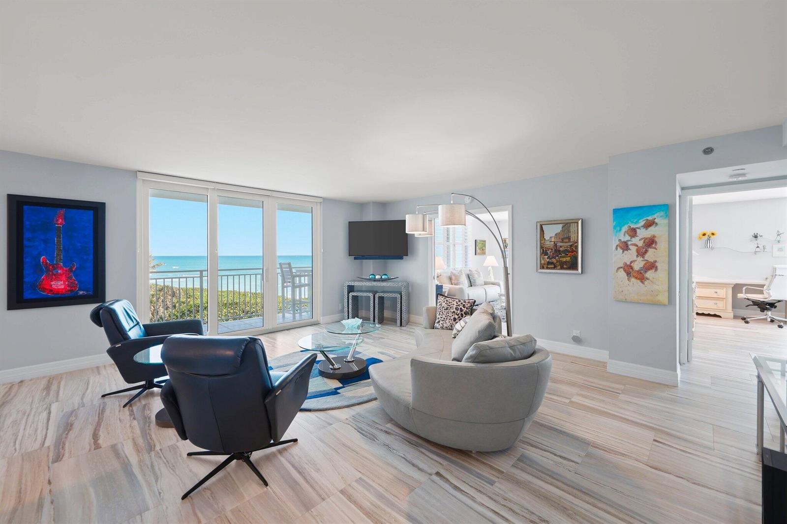 A living room features light wood-look tile floors, a curved sofa, and ocean views — 500 Ocean Drive, Juno Beach FL 33408, JUNO BEACH, FL