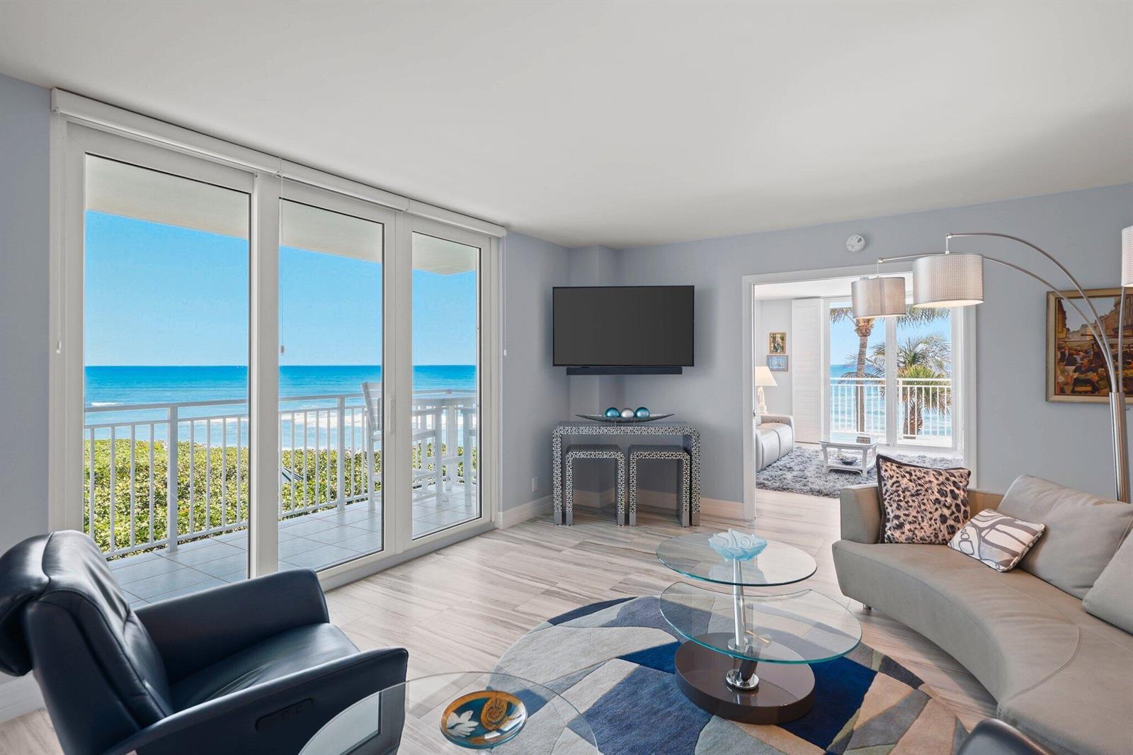 A living room with a curved sofa, glass coffee table, and sliding doors to a balcony — 500 Ocean Drive, Juno Beach FL 33408, JUNO BEACH, FL