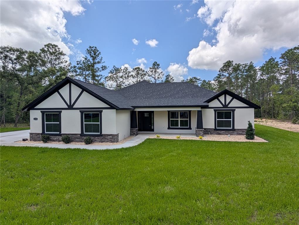 A single-story house with a white stucco facade, dark trim, and stone veneer accents — 12397 SW 76TH LANE, DUNNELLON, FL