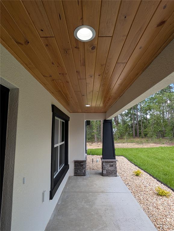 A covered porch features a wood-plank ceiling, recessed lighting, and a stone-based support column — 12397 SW 76TH LANE, DUNNELLON, FL