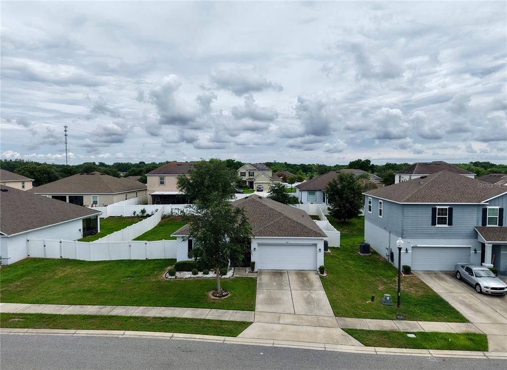 An aerial view shows a suburban neighborhood with single-family homes, white vinyl fences, and lawns — 15280 WHITE TAIL LOOP, MASCOTTE, FL