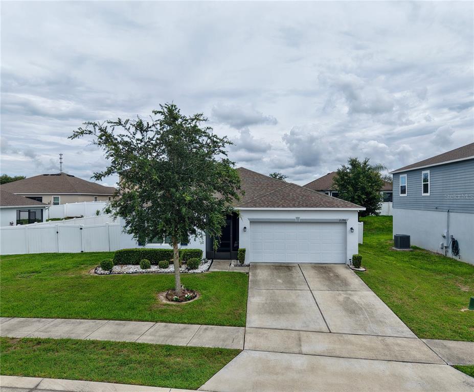 A single-story house with a white garage, a concrete driveway, and a front yard tree — 15280 WHITE TAIL LOOP, MASCOTTE, FL