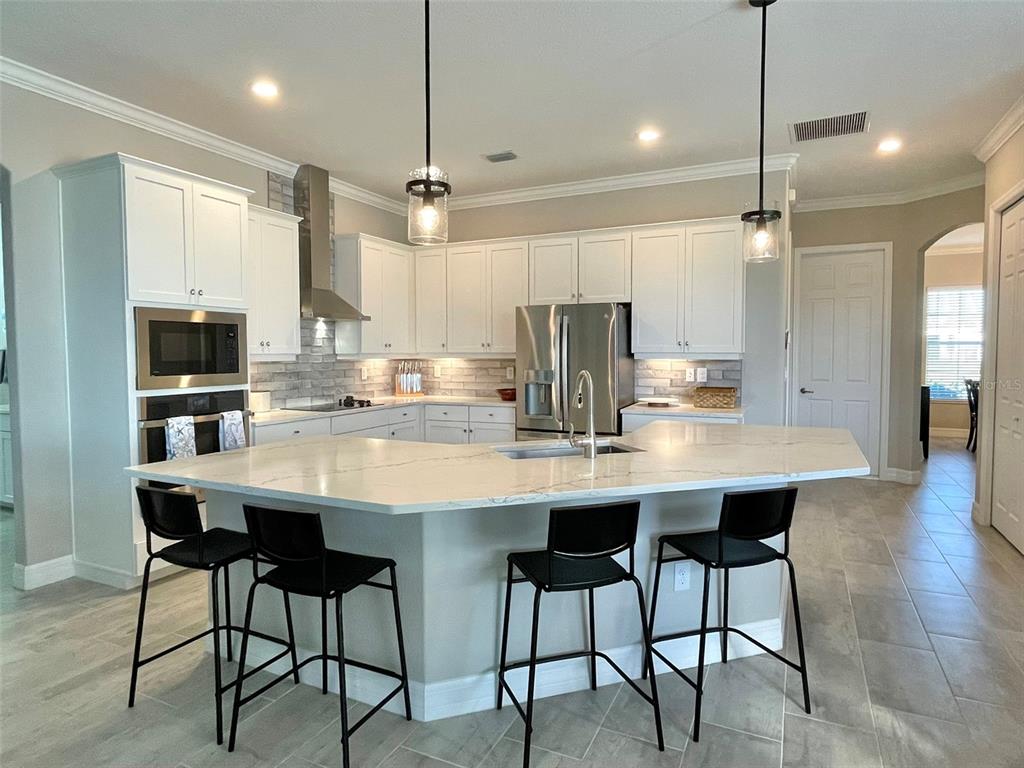 A modern kitchen features white cabinets, stainless steel appliances, a large island, and bar stools — 14580 PONCE DE LEON TRAIL, PORT CHARLOTTE, FL
