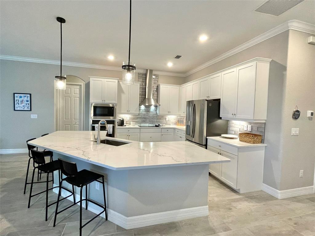 A kitchen features white cabinets, a large quartz-topped island, stainless steel appliances, and pendant lighting — 14580 PONCE DE LEON TRAIL, PORT CHARLOTTE, FL