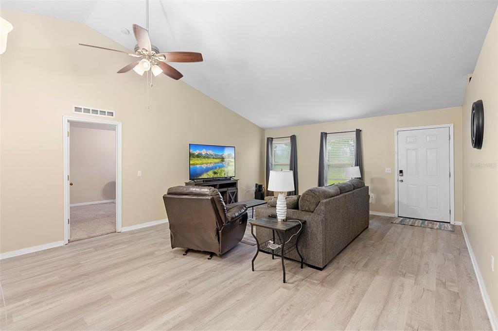 A living room features light wood-look flooring, a vaulted ceiling, a ceiling fan, and furniture — 3750 SW 127TH LANE ROAD, OCALA, FL