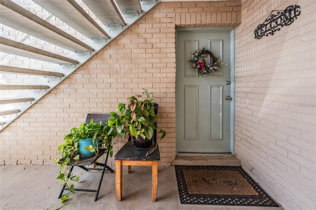 An exterior entryway features a light green door, brick walls, a staircase, and two potted plants — 7210 N MANHATTAN AVENUE UNIT 1913, TAMPA, FL