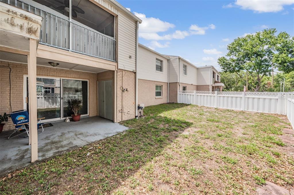 A concrete patio sits beneath a second-story balcony next to a fenced-in grassy yard — 7210 N MANHATTAN AVENUE UNIT 1913, TAMPA, FL