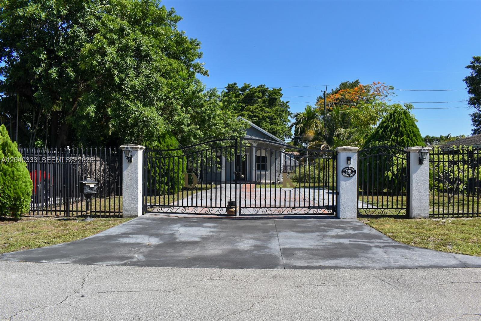 A gated driveway leads to a single-story house surrounded by lush trees and landscaping — 2218 Harding St, Hollywood FL 33020, HOLLYWOOD, FL
