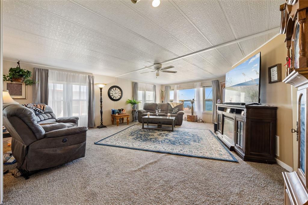 A living room features carpeted floors, a ceiling fan, a television, and a water view — 121 BONNIE DRIVE, AUBURNDALE, FL