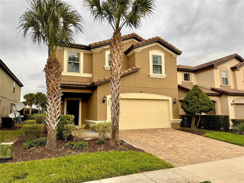 A two-story tan stucco house with a two-car garage and two palm trees in front — 5565 MISTY OAK CIRCLE, DAVENPORT, FL