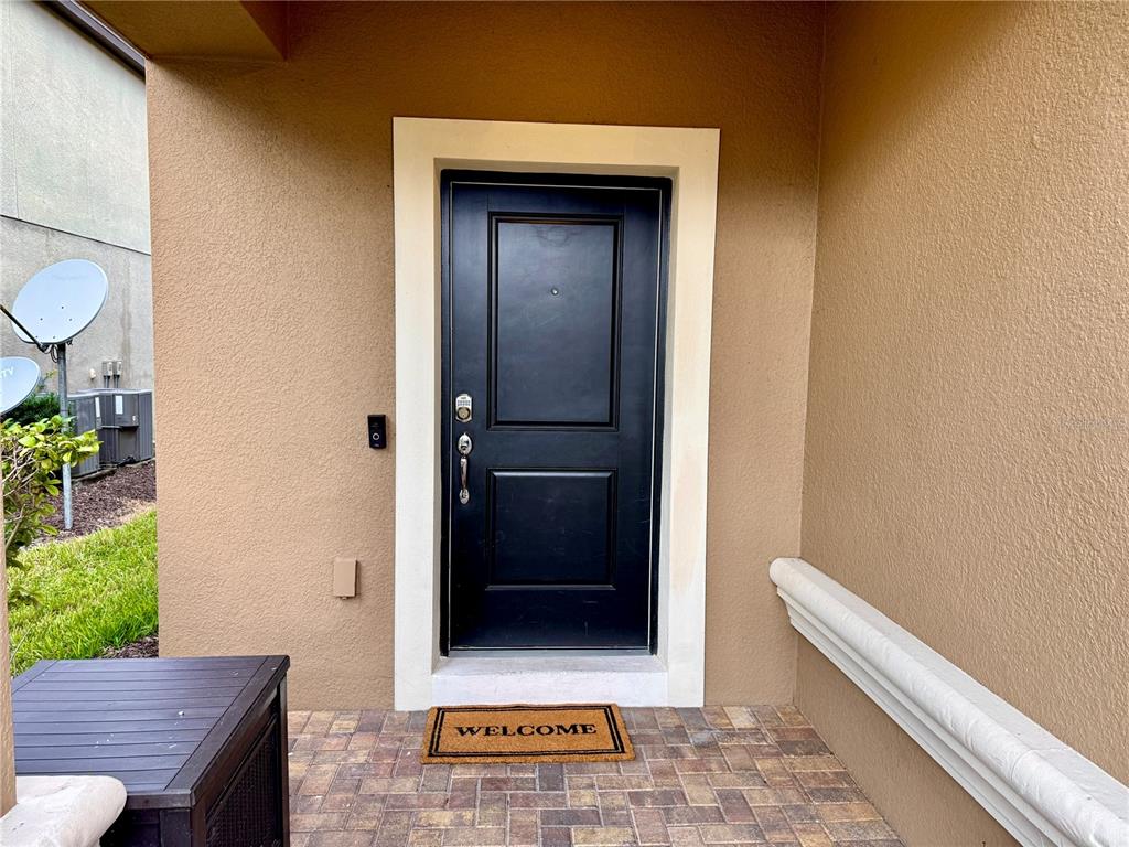 A black front door with a welcome mat sits on a paved porch — 5565 MISTY OAK CIRCLE, DAVENPORT, FL