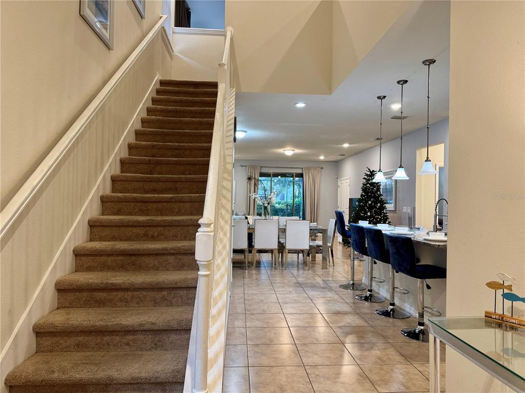 A carpeted staircase leads to an open-concept living area with tile floors and bar seating — 5565 MISTY OAK CIRCLE, DAVENPORT, FL