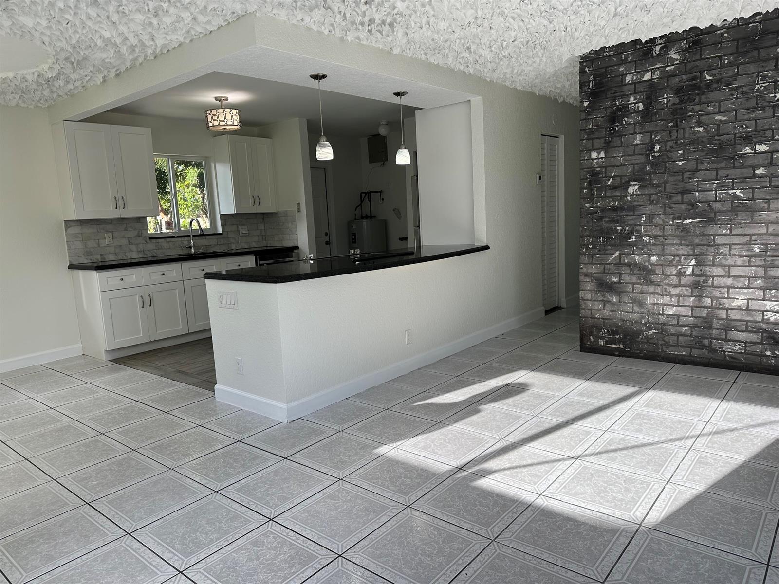 A kitchen with white cabinets and a breakfast bar opens to a tiled living area — 2811 NW 8th Street, Pompano Beach FL 33069, POMPANO BEACH, FL