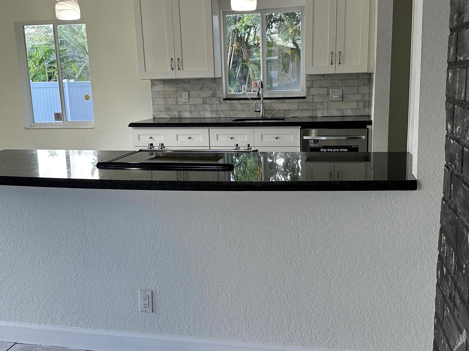 A kitchen features white cabinets, a black countertop, a tiled backsplash, and a breakfast bar — 2811 NW 8th Street, Pompano Beach FL 33069, POMPANO BEACH, FL