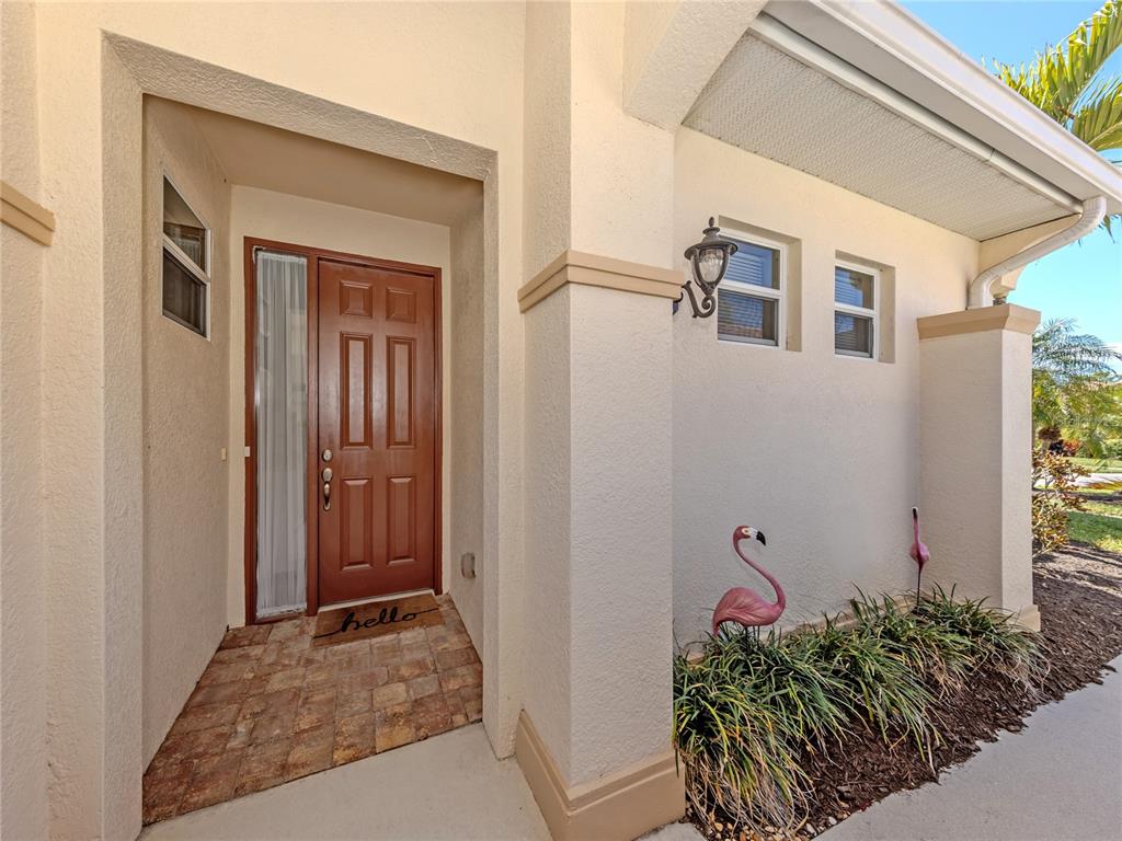 A tan stucco house entrance features a brown front door, tiled porch, and two flamingo statues — 254 MESTRE PLACE, NORTH VENICE, FL