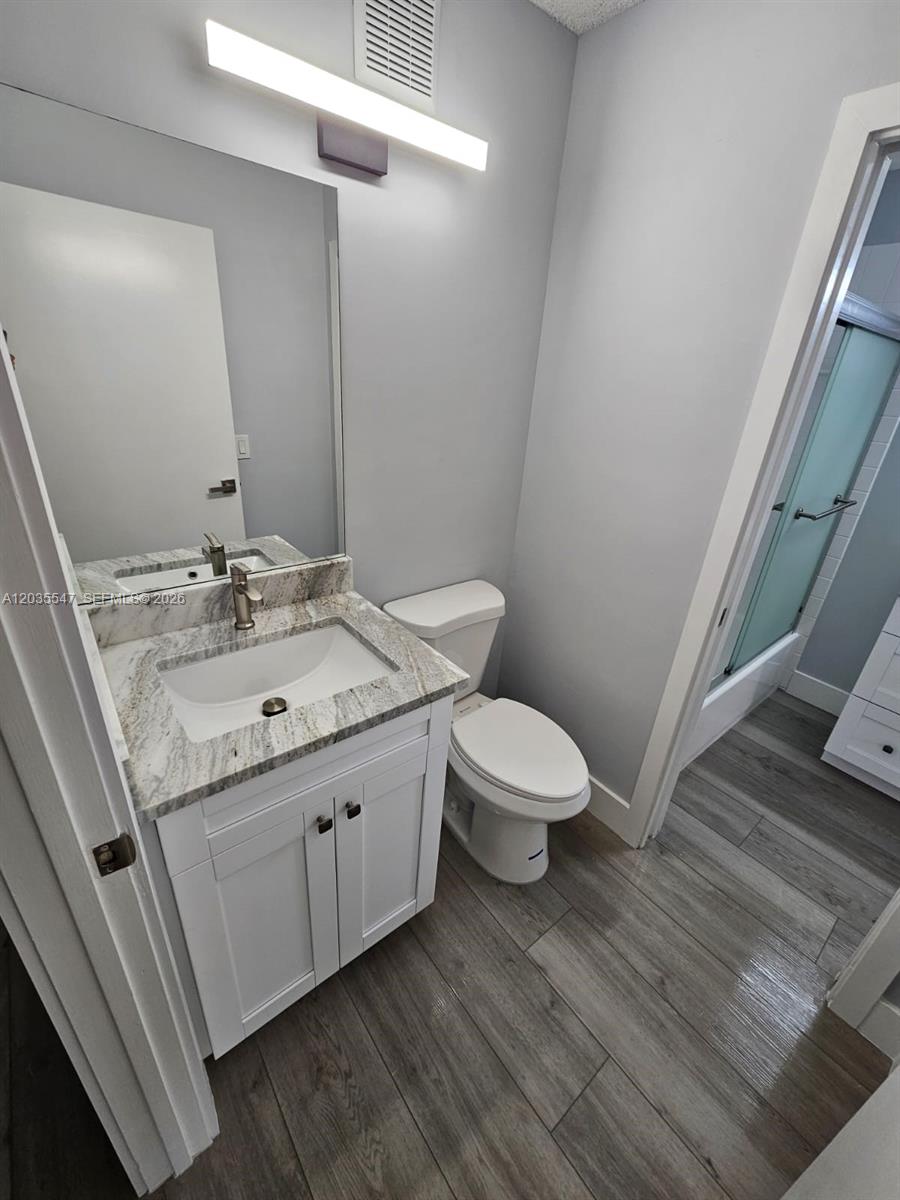 A bathroom features a white vanity with a stone countertop, a toilet, and wood-look flooring — 10823 NW 3rd Ct, Pembroke Pines FL 33026, PEMBROKE PINES, FL