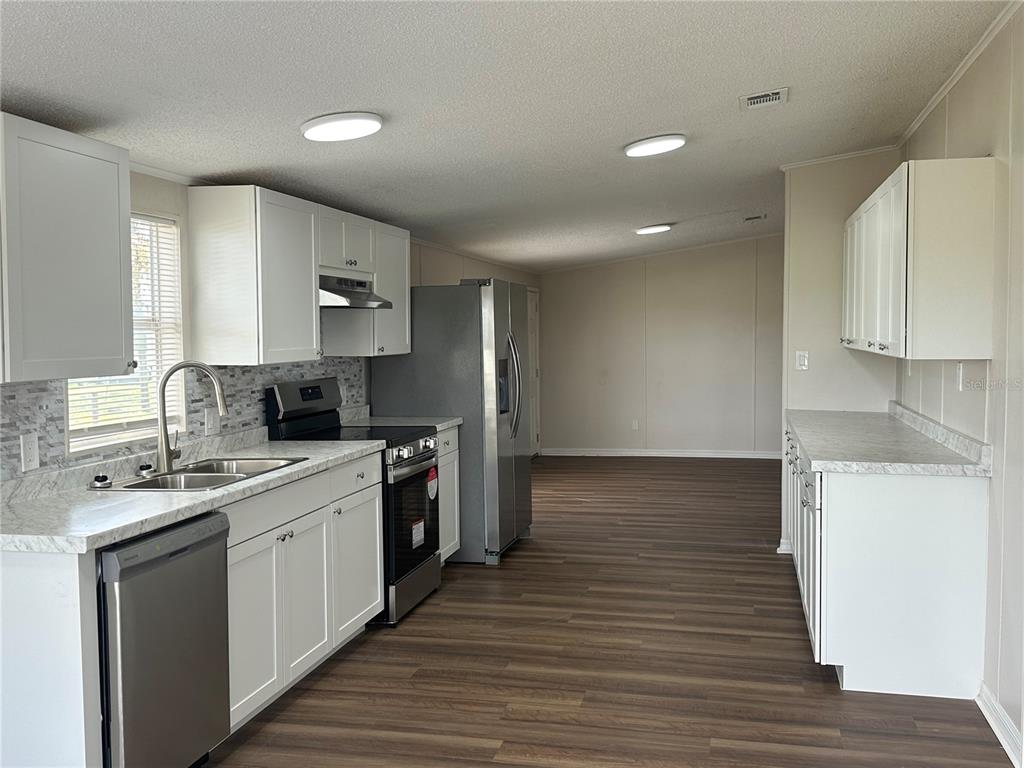 A kitchen with white cabinets, stainless steel appliances, and wood-look flooring in an open space — 4128 W BELLA VISTA STREET, LAKELAND, FL