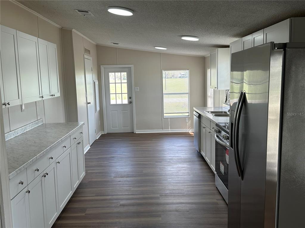 A kitchen features white cabinets, stainless steel appliances, and wood-look flooring — 4128 W BELLA VISTA STREET, LAKELAND, FL