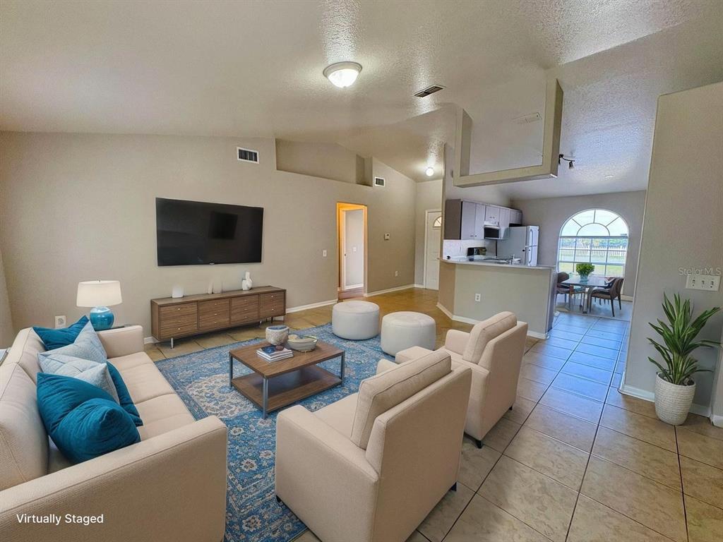 A virtually staged living room with tile flooring, a blue area rug, and an open kitchen — 609 TAMARIN LANE, POINCIANA, FL