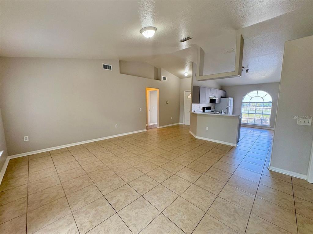 An open-concept living area features light-colored tile flooring, vaulted ceilings, and an adjacent kitchen — 609 TAMARIN LANE, POINCIANA, FL