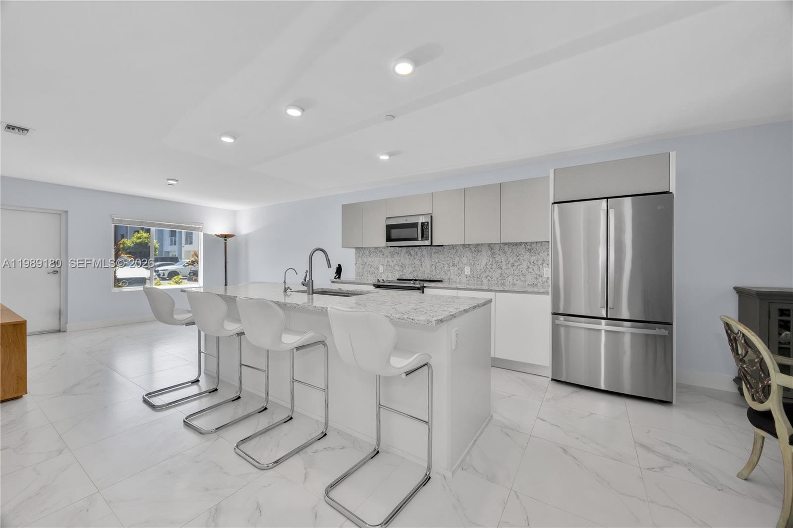 A modern kitchen features a marble-topped island with white bar stools and stainless steel appliances — 2555 NE 193rd St # 2122, Miami FL 33180, MIAMI, FL
